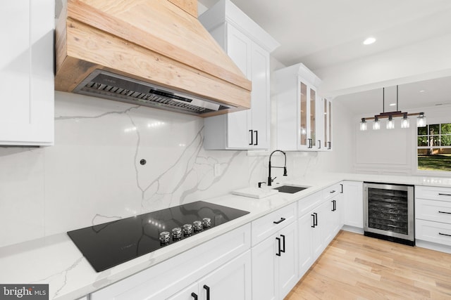 kitchen with light stone countertops, wine cooler, white cabinets, custom range hood, and black electric stovetop