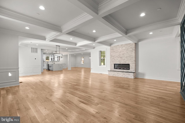 unfurnished living room featuring beam ceiling, light wood finished floors, coffered ceiling, a stone fireplace, and a decorative wall