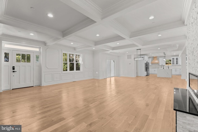 unfurnished living room with light wood finished floors, beam ceiling, coffered ceiling, and a decorative wall