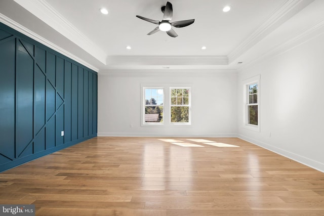 empty room featuring a raised ceiling, light wood finished floors, and ornamental molding