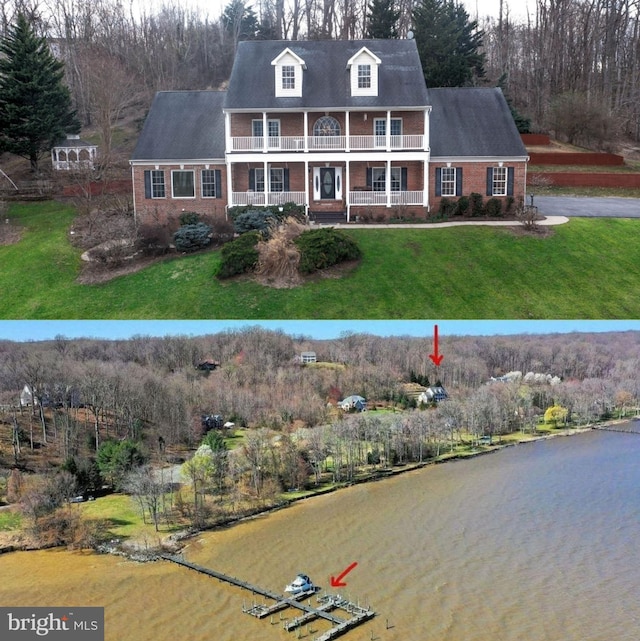 new england style home featuring brick siding, a front lawn, a water view, covered porch, and a balcony