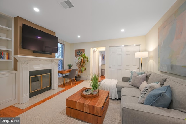 living area with visible vents, built in shelves, a fireplace with flush hearth, recessed lighting, and light wood-style floors