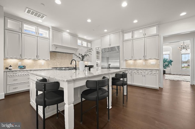 kitchen with visible vents, built in refrigerator, a sink, white cabinetry, and a breakfast bar area