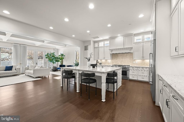 kitchen featuring a breakfast bar area, premium appliances, dark wood-style flooring, white cabinets, and tasteful backsplash