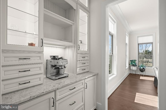 kitchen with dark wood-type flooring, ornamental molding, white cabinetry, baseboards, and light stone countertops