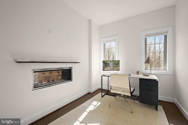 office space featuring a wealth of natural light, a glass covered fireplace, baseboards, and wood finished floors