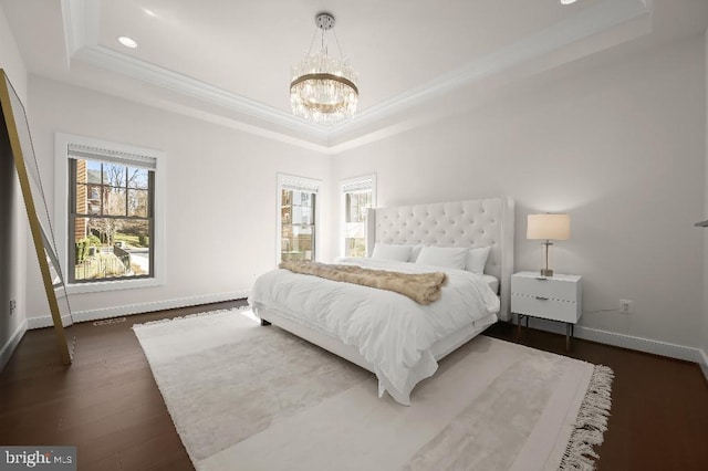 bedroom featuring baseboards, a tray ceiling, dark wood-style flooring, ornamental molding, and a chandelier