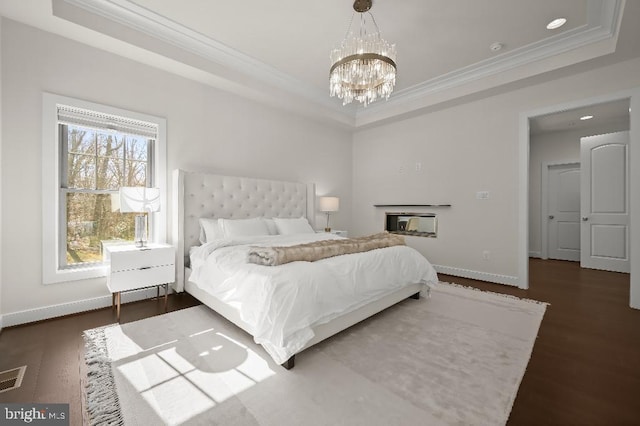 bedroom with a raised ceiling, wood finished floors, and ornamental molding