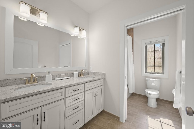 bathroom featuring double vanity, toilet, baseboards, and a sink