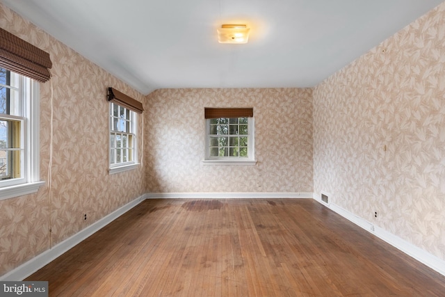 empty room with wallpapered walls, a healthy amount of sunlight, visible vents, and hardwood / wood-style floors