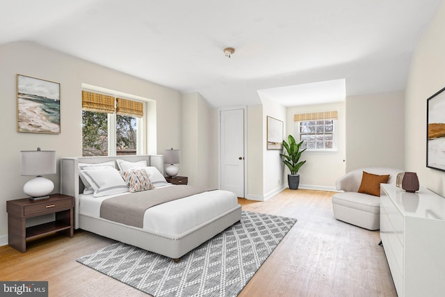 bedroom featuring baseboards, light wood-style floors, and vaulted ceiling