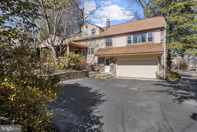 view of front of house featuring a garage, stone siding, a chimney, and driveway