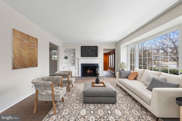 living room with built in features, a fireplace with flush hearth, baseboards, and wood finished floors