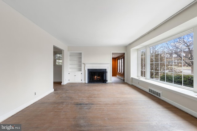 unfurnished living room featuring wood finished floors, visible vents, plenty of natural light, and built in shelves