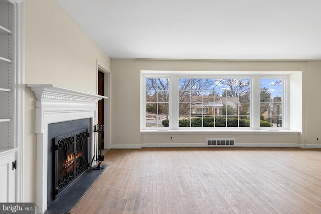 unfurnished living room with visible vents, a healthy amount of sunlight, a fireplace with flush hearth, and wood finished floors