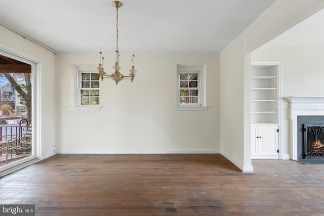 unfurnished dining area with a warm lit fireplace, baseboards, built in shelves, and wood finished floors