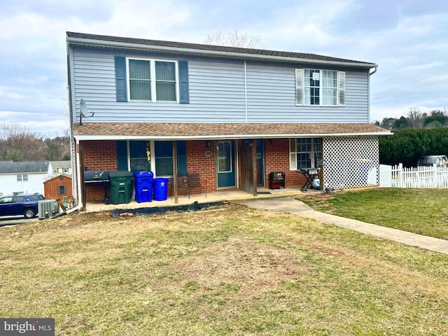 view of front of house with fence, roof with shingles, covered porch, a front lawn, and brick siding