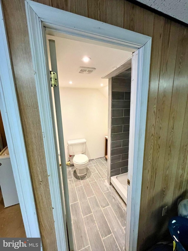 full bathroom with visible vents, a shower stall, wood tiled floor, wood walls, and toilet