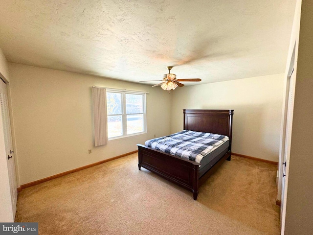 bedroom with a textured ceiling, a closet, baseboards, light colored carpet, and ceiling fan