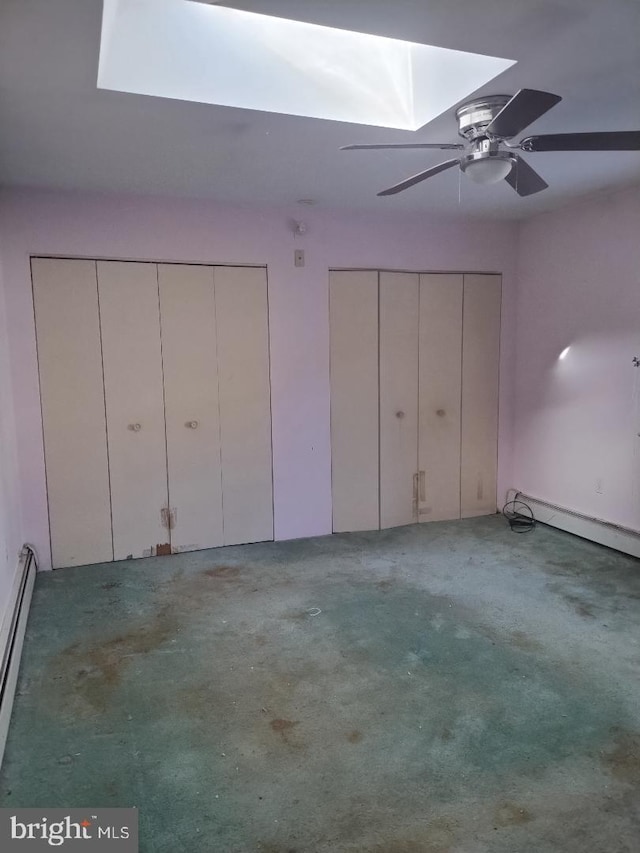 interior space featuring multiple closets, carpet, a skylight, baseboard heating, and ceiling fan