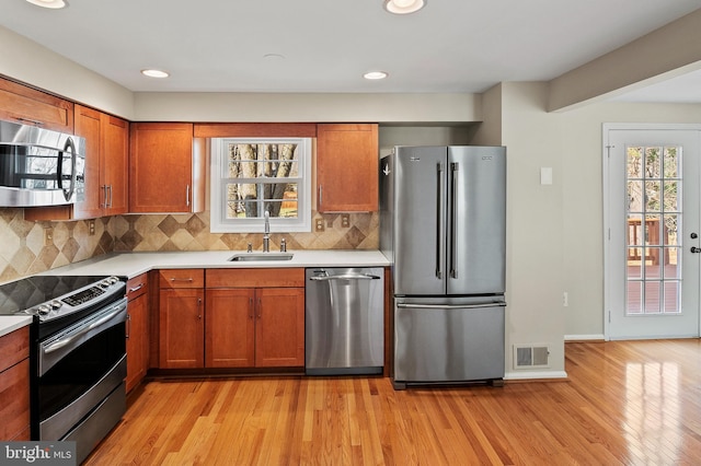 kitchen featuring light countertops, appliances with stainless steel finishes, light wood-style floors, brown cabinetry, and a sink