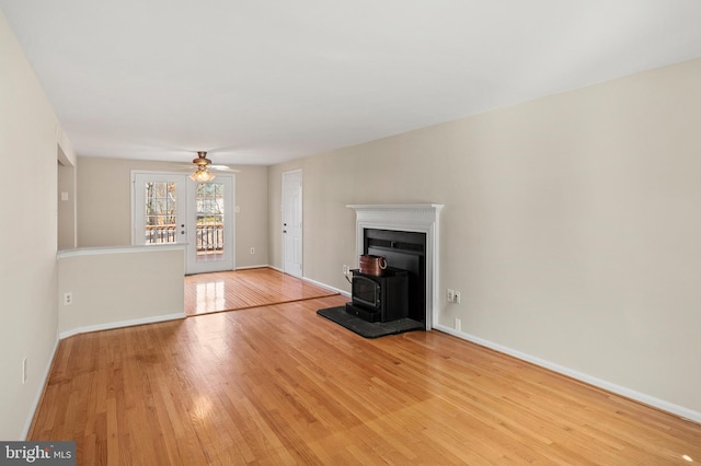 unfurnished living room with a ceiling fan, light wood-type flooring, baseboards, and a wood stove