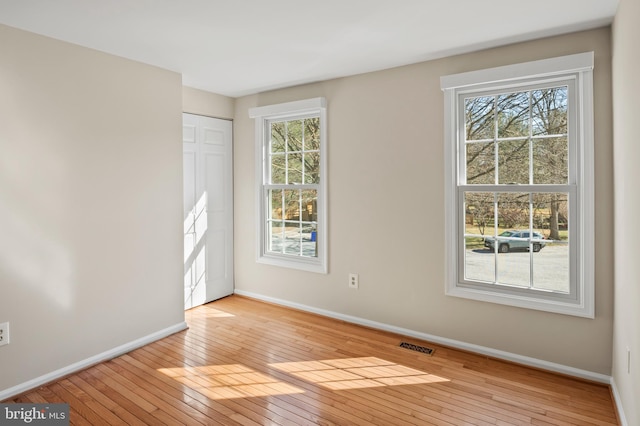 unfurnished room with hardwood / wood-style flooring, visible vents, and baseboards