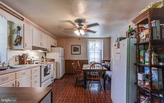 kitchen with a wainscoted wall, under cabinet range hood, a sink, white cabinetry, and white appliances