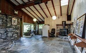 interior space featuring a wood stove, wood walls, vaulted ceiling with beams, and stone finish flooring