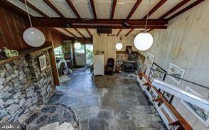 unfurnished living room with beamed ceiling, stone finish floor, and a wood stove