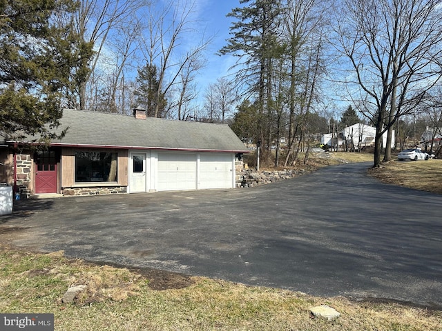 view of side of home with aphalt driveway, stone siding, an attached garage, and a chimney