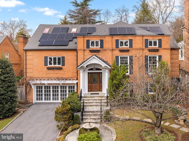 view of front of home with solar panels, aphalt driveway, an attached garage, and brick siding