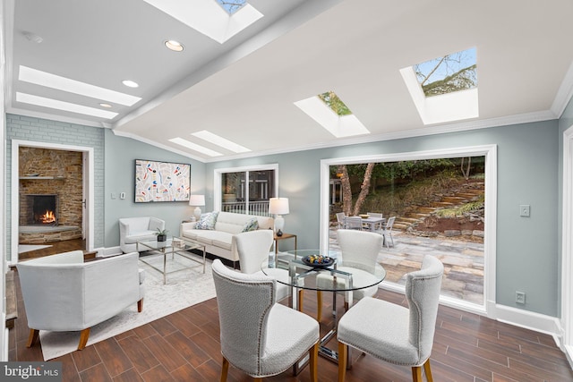 living area featuring lofted ceiling with skylight, ornamental molding, a fireplace, and wood finish floors