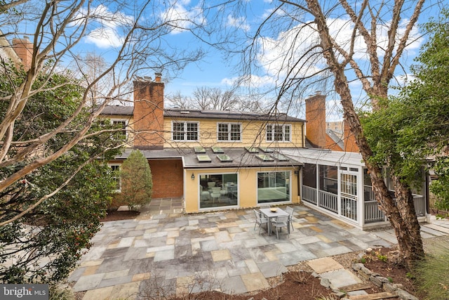 rear view of property with a sunroom, a chimney, and a patio area