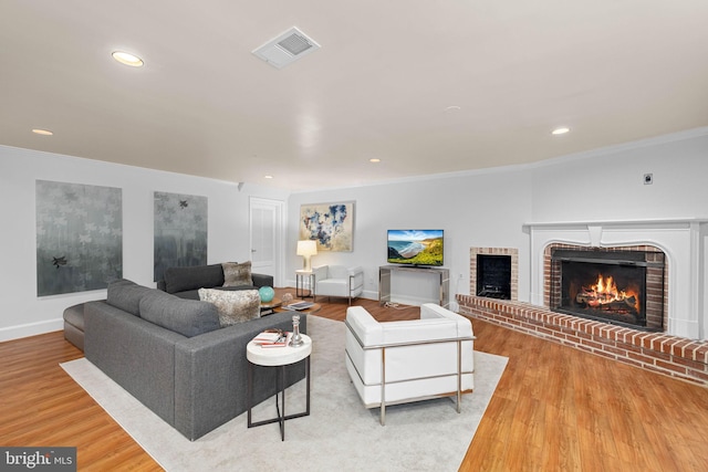 living room featuring visible vents, wood finished floors, a fireplace, and ornamental molding