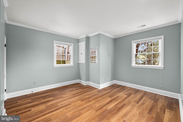 empty room featuring visible vents, crown molding, baseboards, and wood finished floors