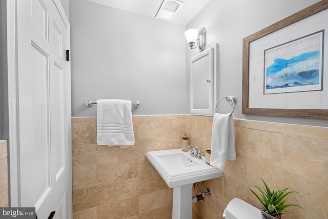 bathroom featuring visible vents, toilet, tile walls, and wainscoting