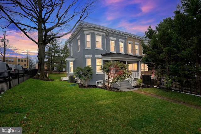 back of property at dusk with a yard, fence, covered porch, and central AC