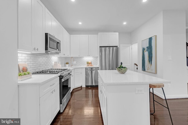 kitchen with dark wood-style floors, a kitchen island, appliances with stainless steel finishes, a kitchen breakfast bar, and backsplash