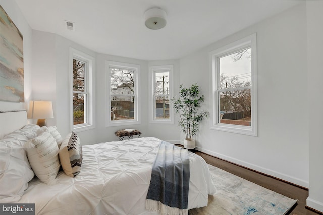 bedroom featuring wood finished floors, multiple windows, baseboards, and visible vents