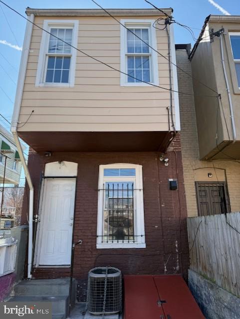 view of front of property featuring brick siding, central AC unit, and fence