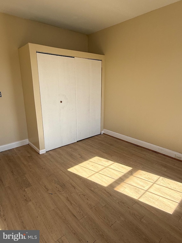 unfurnished bedroom featuring wood finished floors, baseboards, and a closet