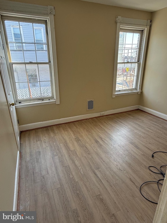 empty room with visible vents, plenty of natural light, baseboards, and wood finished floors