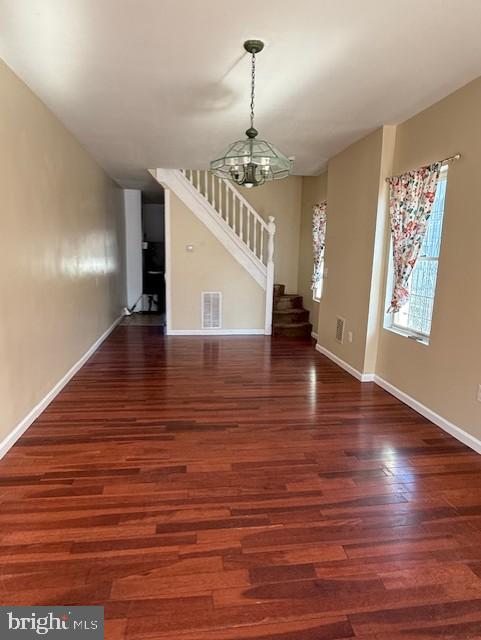 unfurnished living room with visible vents, wood finished floors, an inviting chandelier, baseboards, and stairs