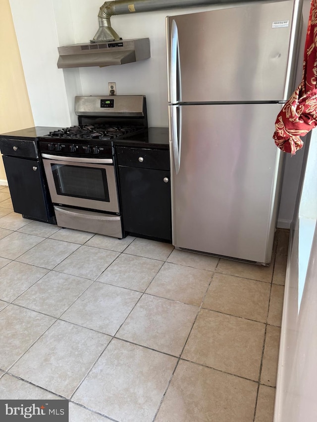 kitchen with under cabinet range hood, light tile patterned floors, dark countertops, and appliances with stainless steel finishes