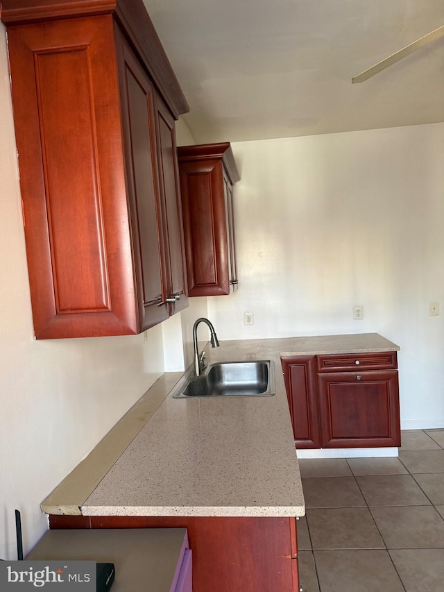 kitchen featuring tile patterned floors, light stone counters, reddish brown cabinets, and a sink