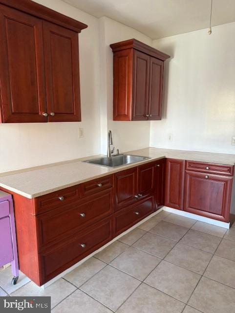 kitchen featuring light countertops, light tile patterned floors, dark brown cabinets, and a sink