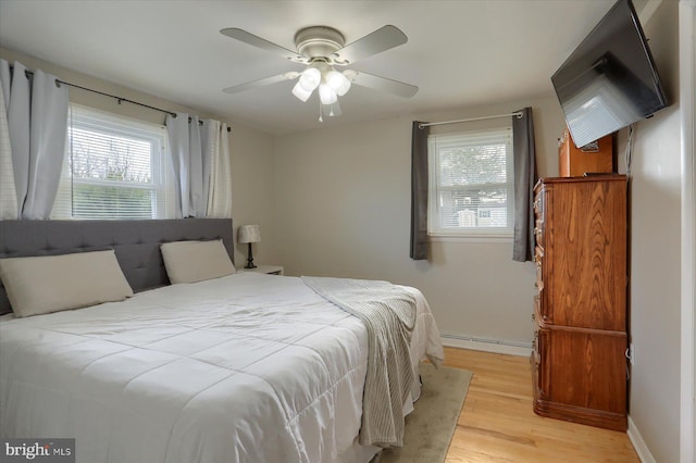 bedroom featuring baseboard heating, ceiling fan, baseboards, and light wood-style floors