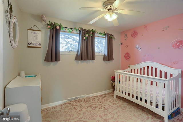 bedroom featuring visible vents, a crib, baseboards, and a ceiling fan