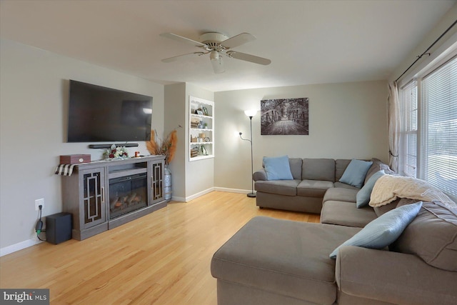 living room with a glass covered fireplace, baseboards, wood finished floors, and a ceiling fan